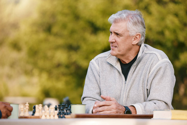 Starszy mężczyzna, park i myślenie o szachy, gra i konkurencja przy stole przez drzewa, słońce i skupienie. Starszy szachista, odkryty i strategia konkursu w przyrodzie, relaks i grać w Los Angeles. - Zdjęcie, obraz