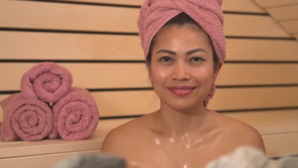 PORTRAIT: Uśmiechnięta młoda Azjatka leczona sauną fińską w centrum odnowy biologicznej. Terapia saunowa w celu detoksykacji, łagodzenia stresu i wzmocnienia układu odpornościowego w zimnych jesiennych miesiącach. - Materiał filmowy, wideo