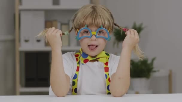 Chica divertida de 7 años vestida con gafas de payaso, mariposa y tirantes. Imágenes de alta calidad 4k - Metraje, vídeo