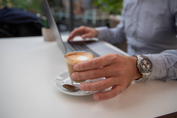 Egy üzletember kávézik, miközben a laptopján dolgozik, közelkép a kezéről. - Fotó, kép