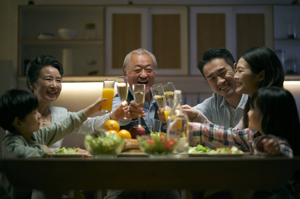 trzypokoleniowe azjatyckie rodziny zbierające się w domu świętując święto wznosząc toast - Zdjęcie, obraz