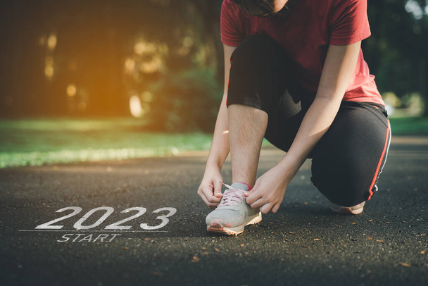 Sport femme runner lacets début de la nouvelle année 2023. Démarrage de la coureuse courir sur la piste de course de la nature aller à l'objectif de succès. Les gens qui courent dans le cadre du numéro 2023. Soins de santé sportive. - Photo, image