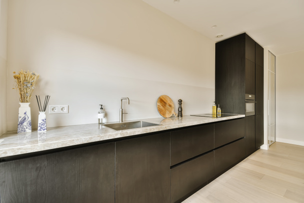 een moderne keuken met zwarte kasten en witte aanrechtbladen in het midden van de kamer is een grote spiegel aan de muur - Foto, afbeelding
