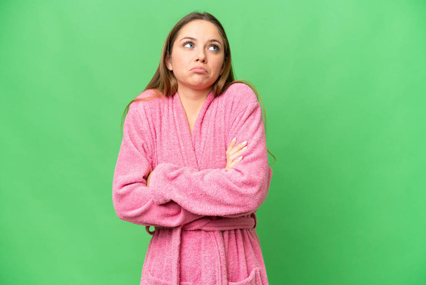 Young woman in a bathrobe over isolated chroma key background making doubts gesture while lifting the shoulders - Fotografie, Obrázek
