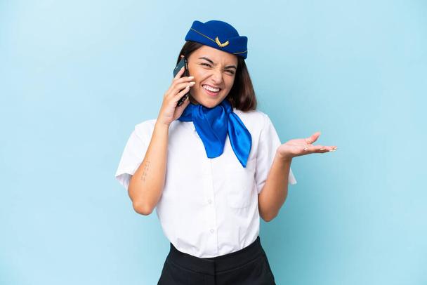 Repülőgép stewardess kaukázusi nő elszigetelt kék háttér miközben egy beszélgetést a mobiltelefon valakivel - Fotó, kép