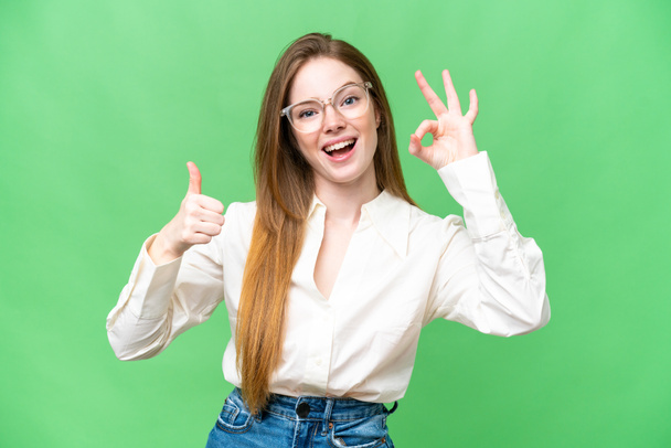 Молодая красивая женщина на изолированном фоне хрома ключ показывая хорошо знак и большой палец вверх жест - Фото, изображение