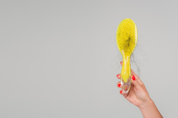 cropped view of woman with red manicure holding yellow hair brush with lost hair isolated on grey - Foto, Imagen