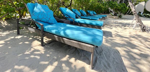 Lounge krzesła lub krzesła plażowe na białym piasku plaży w gorący letni dzień w luksusowym tropikalnym hotelu lub ośrodku. Podróże, turystyka, wakacje, koncepcja wakacji. Palmy, zieleń - Zdjęcie, obraz