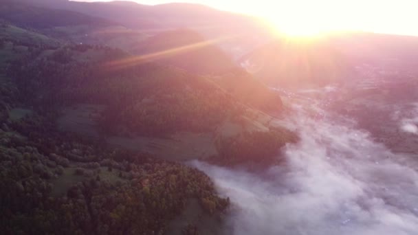 Légi drón kilátás köd és inverziós felhők egy vidéki völgyben egy hegyvidéki táj a Kárpátok, napkeltekor. Fényes Nap emelkedik fel a hegyek mögül. FHD drón videó - Felvétel, videó