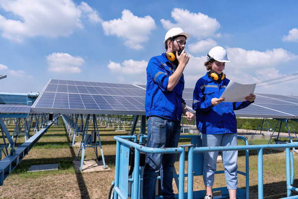 Ingenieros de mantenimiento en el puesto de granja solar en elevador de tijeras, inspección de paneles solares e informes de radio  - Foto, imagen