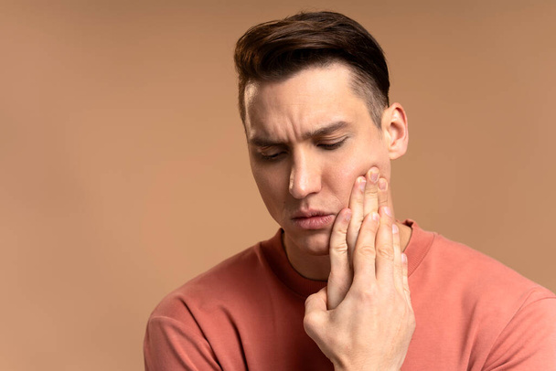 Problemy z zębami. Portret niezdrowego mężczyzny naciskającego ból policzka, cierpiącego na ostry ból zęba, chorobę przyzębia, ubytki lub ból szczęki. kryty studio strzał izolowany na beżowym tle  - Zdjęcie, obraz