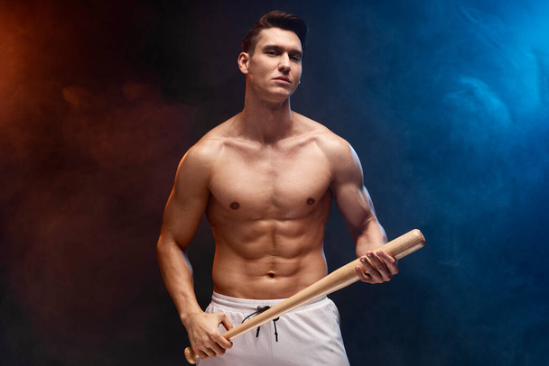 Strong and fit man bodybuilder with baseball bat posing with naked torso. Sporty muscular guy athlete. Sport and fitness concept - Photo, Image