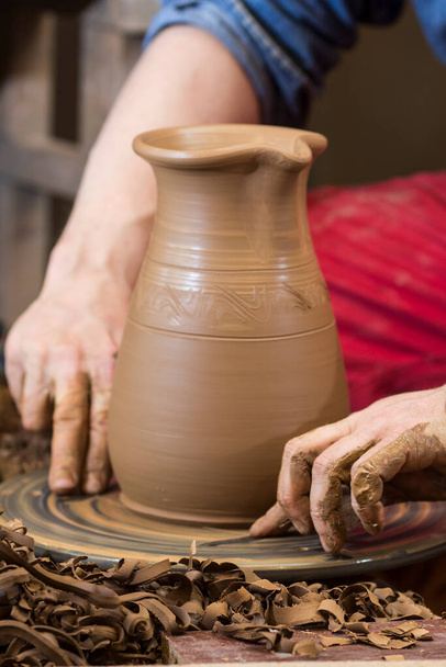 руки горшечника работают с глиной на гончарном колесе, образуя чашу. Традиционная керамика, ремесла, аутентичная атмосфера - Фото, изображение
