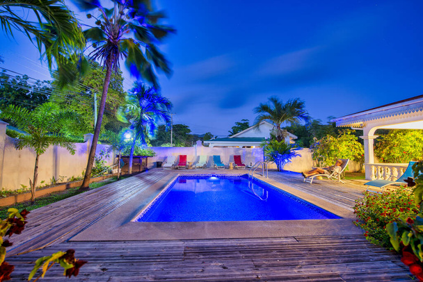 Νυχτερινή θέα ενός τροπικού σπιτιού με πισίνα και φοίνικες. - Φωτογραφία, εικόνα