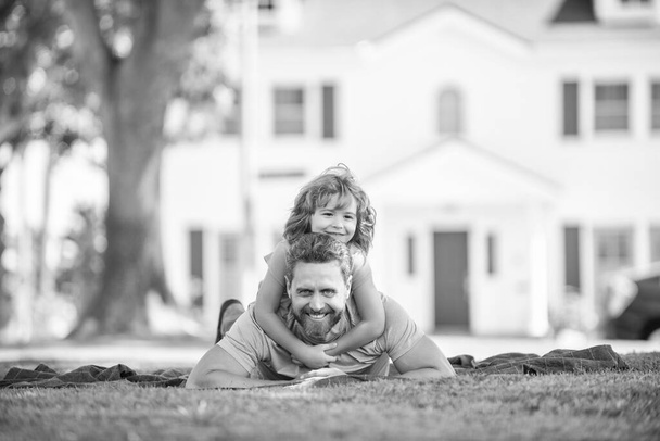 Ευτυχισμένος πατέρας διασκεδάζοντας με το παιδί χαλαρώστε μαζί στο πράσινο γρασίδι πάρκο, φίλοι. - Φωτογραφία, εικόνα