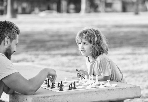 happy family of dad and son boy playing chess on table in park outdoor, chess competition. - Foto, immagini