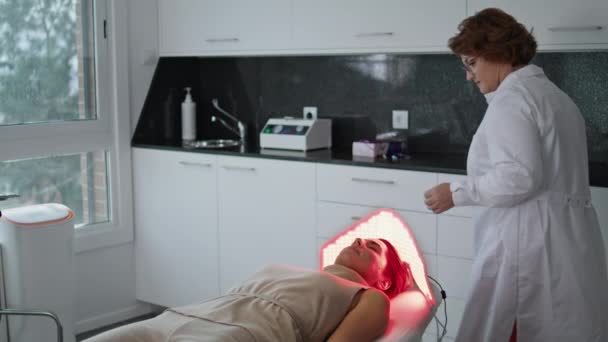 Σύγχρονη κοσμετολογία φωτοδυναμική θεραπεία για την αναζωογόνηση του δέρματος σε κλινική ομορφιάς. Επαγγελματίας κοσμετολόγος ρύθμιση εξοπλισμού φωτοθεραπείας με λαμπτήρες LED. Αντιγηραντική διαδικασία περιποίησης στο spa salon - Πλάνα, βίντεο