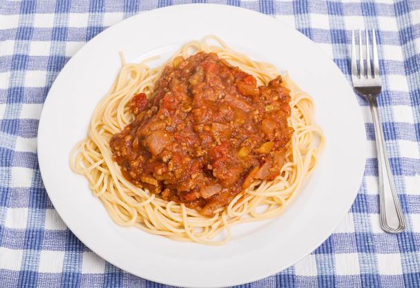 Plaat van Spaghetti en vlees saus op blauwe geruite Placemat - Foto, afbeelding