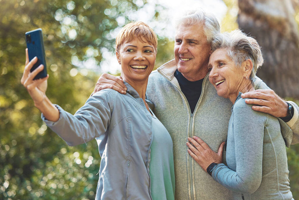 Selfie ze smartfonem, osobami starszymi i przyjaciółmi uśmiecha się na świeżym powietrzu z emerytury i fitness w parku z fotografii komórkowej. Telefon komórkowy, szczęśliwy na zdjęciu z seniorami w naturze - Zdjęcie, obraz