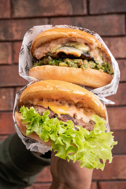 Hand holding delicious hamburgers on a brick background - Foto, Imagen
