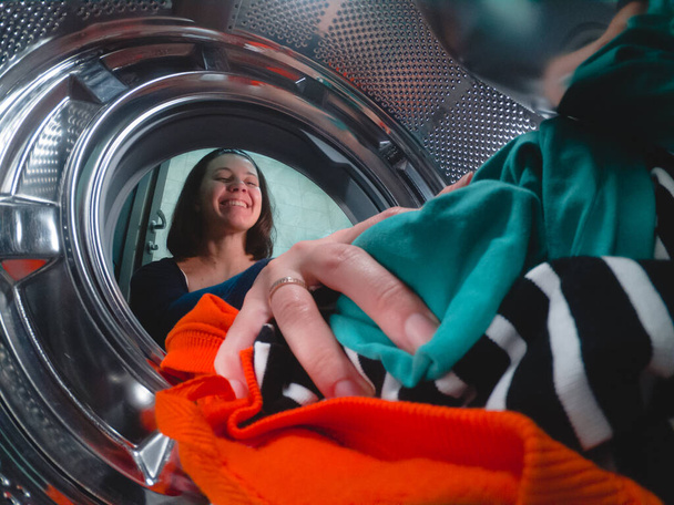 uma mulher carrega uma máquina de lavar roupa com roupas sujas - Foto, Imagem