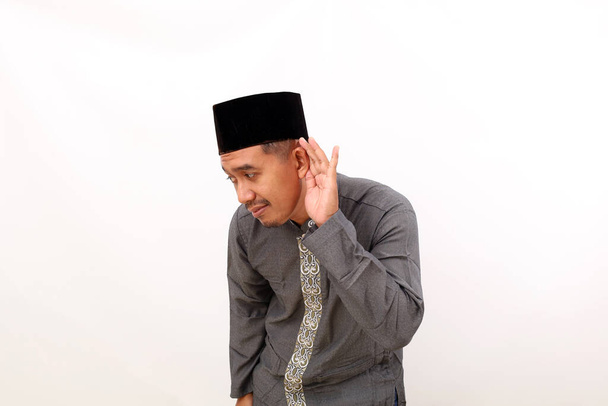 Asiatischer muslimischer Mann im Stehen, während er sein Ohr hält, um etwas zu hören. Isoliert auf weißem Hintergrund - Foto, Bild