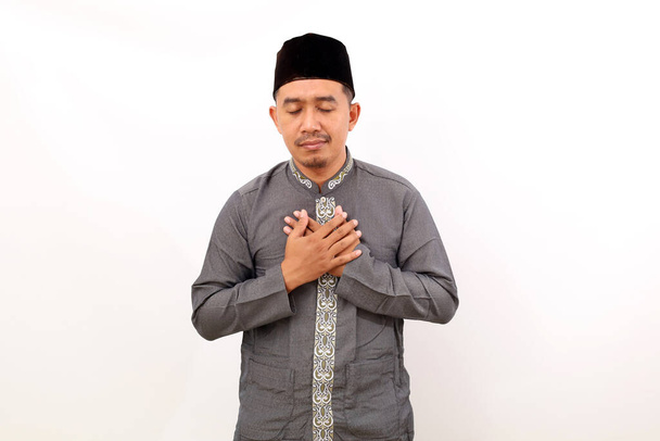 Alleviato rilassato uomo musulmano asiatico in piedi tenendo il petto e chiudendo gli occhi. Isolato su sfondo bianco - Foto, immagini
