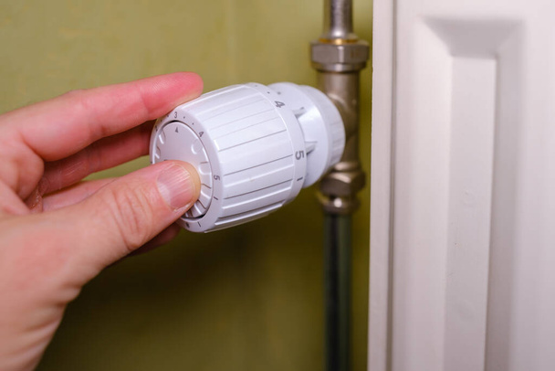 Aumento de los costos de calefacción en crisis, el hombre regula la temperatura en el hogar con el termostato de calefacción para ahorrar energía, primer plano - Foto, Imagen