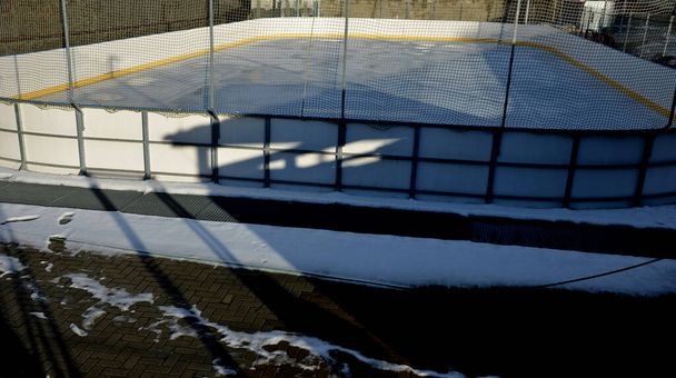 Hockeyfeld, öffentliches Eislaufen im Freien und Unterricht für kleine Kinder mit einem Lehrer. Gelbe Linie um die Leitplanken. Der Park außerhalb der Stadt verwandelt sich in eine Eisbahn. Leere neue modifizierte Motorschlitten - Foto, Bild