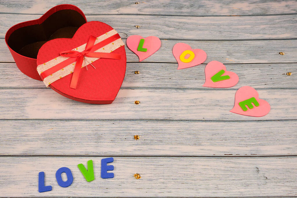 Rode hartvormige doos bovenop een blauwe houten tafel, met hartjes met het woord liefde. Liefde, Valentijnsdag concept. - Foto, afbeelding