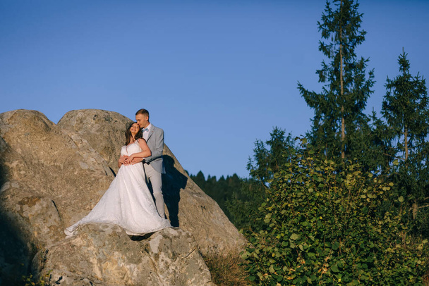 Красива пара молодят, наречена і наречений у весільних сукнях, що йдуть на тлі гір
 - Фото, зображення