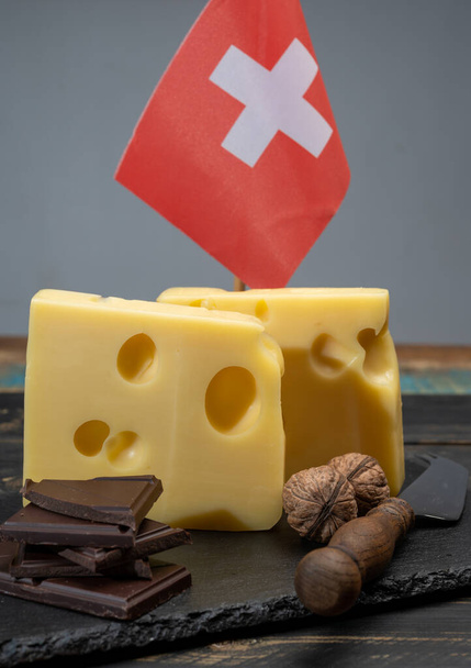 Schweizer Lebensmittel, mittelharter Kuhmilchkäse emmentaler mit Löchern, dunkle Schweizer Schokolade und Schweizer Flagge aus nächster Nähe - Foto, Bild