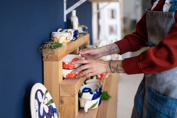 Close up view of pottery studio owner putting mug at right place. Ceramist girl tidies up the shelves with handcraft ceramics at her studio. Small business and female artist entrepreneur concept - Fotoğraf, Görsel