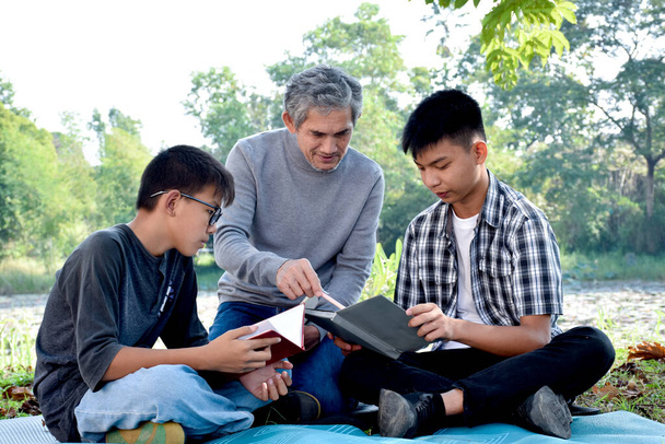 アジアの高齢者や孫たちは、彼らが幸せに、柔らかく、選択的な焦点に興味を持っている本のトピックについて教えたり、読んだり、話したりすることで、公園で一緒に時間を過ごしていますファーストボーイ. - 写真・画像