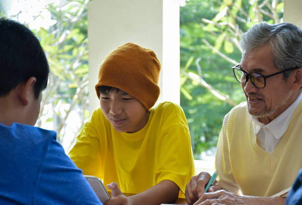 Asian elderly male teacher is helping students to do the school project work by teaching the correct order and process of doing research projects and Internet reference resources. - Foto, Imagem