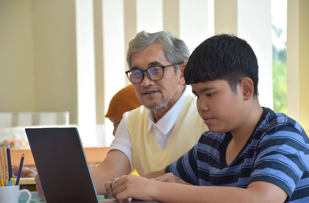 Asian boys are sitting infront of asian elderly teacher inside the room to ask and to do the school project work and listening to the elderly teacher about their project work, soft and selective focus - Foto, Imagem
