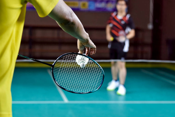 El jugador de bádminton sostiene la raqueta y el volante de crema blanca frente a la red antes de servirlo en otro lado de la cancha. - Foto, imagen