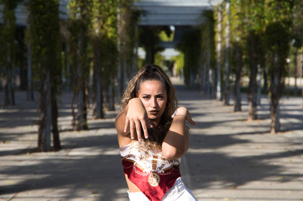 Latin woman, young and beautiful dancing modern dance in the street in a park and makes different expressions and postures. Concept dance, hip hop, dance, art, action, beauty, youth art. - Foto, Imagen