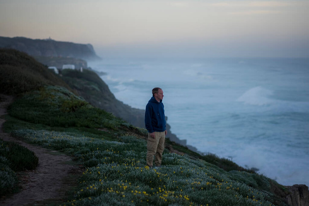 Bir adam okyanus kıyısında sabah sörfünün arka planına karşı duruyor..  - Fotoğraf, Görsel