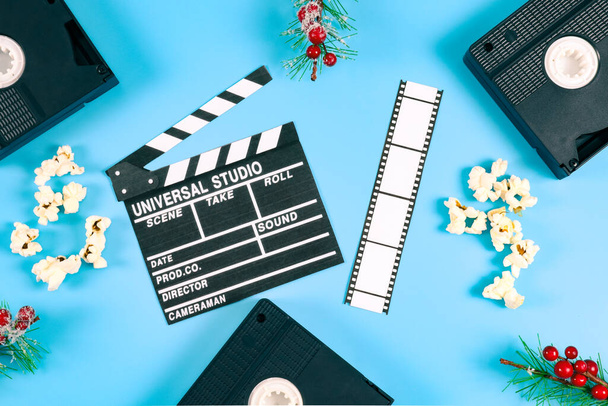 Kolme retro-videonauhaa, kuusen oksat punaisilla marjoilla, limppu ja popcornia sinisellä taustalla, lähikuva ylhäältä. Elokuvan käsite, joulu. - Valokuva, kuva