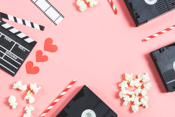A clapperboard, film szalag, szívószálak, popcorn és papír piros szív fekszik egy keret egy rózsaszín háttér egy másolatot a hely a központban, felső nézet közelkép. Mozi szerelem és Valentin-napi koncepció. - Fotó, kép