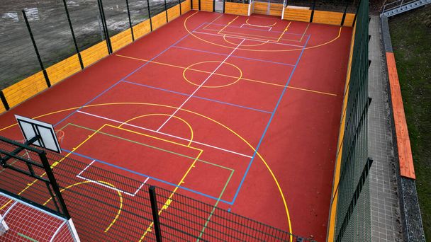 wielofunkcyjny odkryty plac zabaw dla gry w piłkę w szkole. zielony sztuczna trawa z plastikowego dywanu z linii. obręcze do koszykówki i piłki nożnej. wokół chwytając wysoką sieć i poręcze  - Zdjęcie, obraz