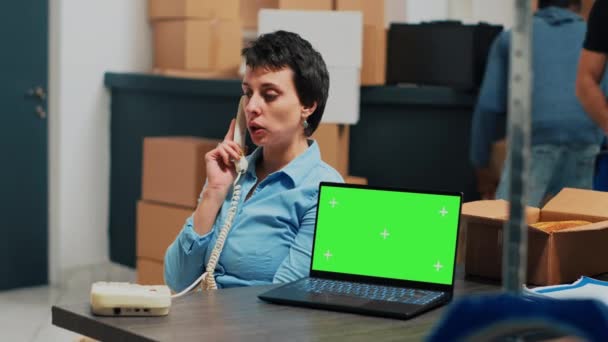 Γυναίκα υπάλληλος που μιλάει στο σταθερό τηλέφωνο έχει οθόνη στο laptop, χρησιμοποιώντας το τηλέφωνο γραφείου για να στείλει το πακέτο εμπορευμάτων. Γυναίκα που εργάζεται σε αποστολή παραγγελιών αγαθών, εφοδιαστική αλυσίδα. - Πλάνα, βίντεο
