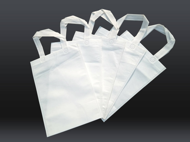 weiße Vliesbeutel auf schwarzem Hintergrund. Reduzieren Sie die Wiederverwendung von Recyclingtüten. Nur wenige umweltfreundliche Stofftaschen. - Foto, Bild
