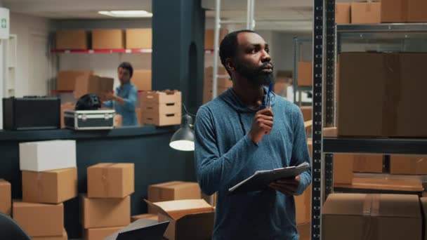 Afro-Amerikaanse werknemer het nemen van inventaris notities op klembord papieren, het controleren van de kwaliteit van producten en pakketten. Jonge volwassene op zoek naar kartonnen dozen, merchandise stock logistiek. - Video