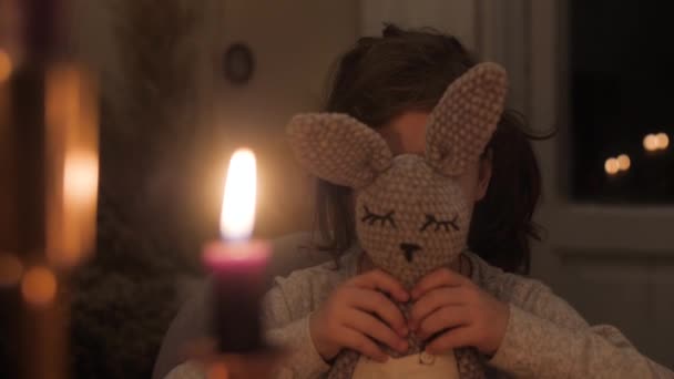 портрет 7-летней девочки, которая прячется за мягким игрушечным зайцем, опускает его и улыбается в камеру, что дает понять, что у ребенка отсутствует один передний зуб - Кадры, видео