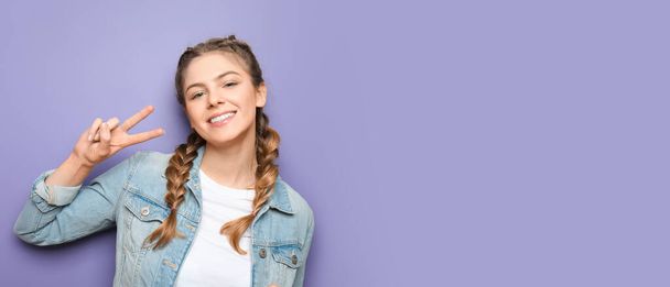 Beautiful young woman showing victory gesture on violet background with space for text - Foto, Imagen