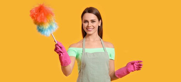 Young housewife with dust brush on yellow background - Photo, image