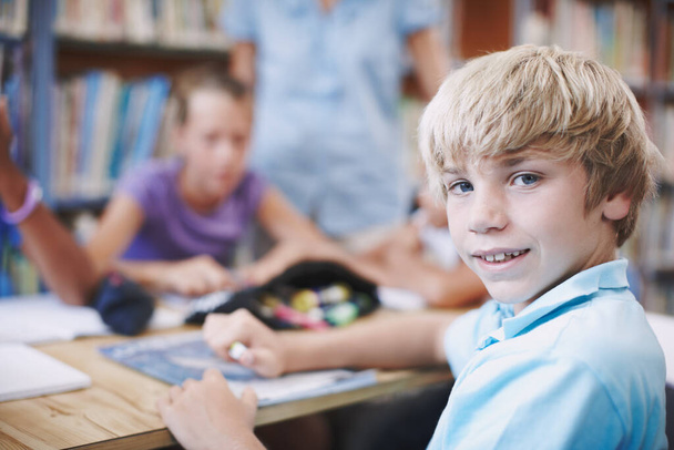 Τα νεαρά μυαλά είναι ώριμα για μάθηση. Ένα νεαρό αγόρι που κοιτάει πίσω του ενώ είναι στη βιβλιοθήκη με τους συμμαθητές του. - Φωτογραφία, εικόνα
