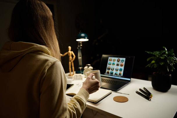 女性は自宅のオフィスで仕事をするのが遅い。夜のリビングルームでノートパソコンを使用してヘッドフォンを身に着けている女性 - 写真・画像